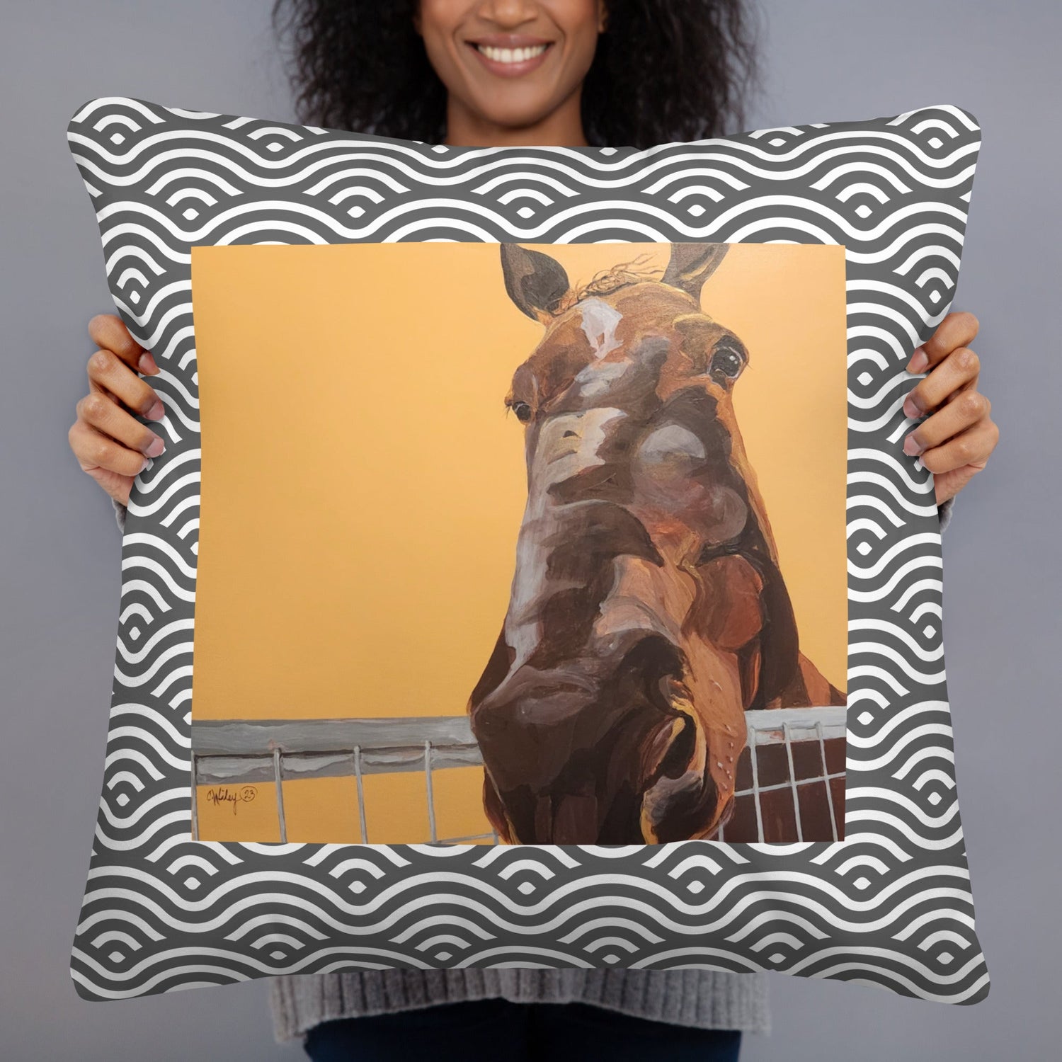 A woman holding a pillow with a brown horse on an orange background, framed by black and white wavy pattern.