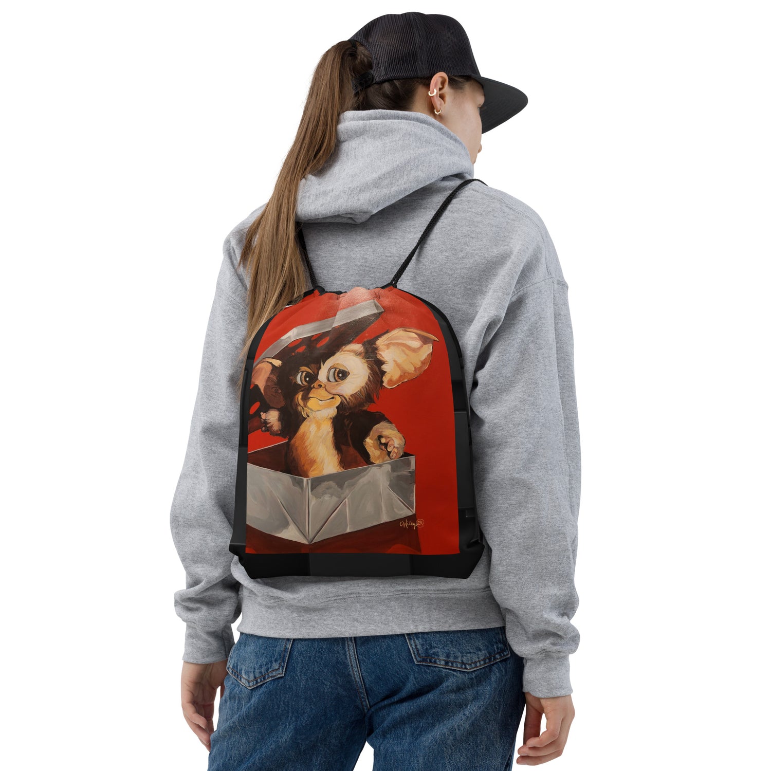 A woman in a cap and sweatshirt wearing a drawstring bag that features Gizmo the Gremlin on her back.