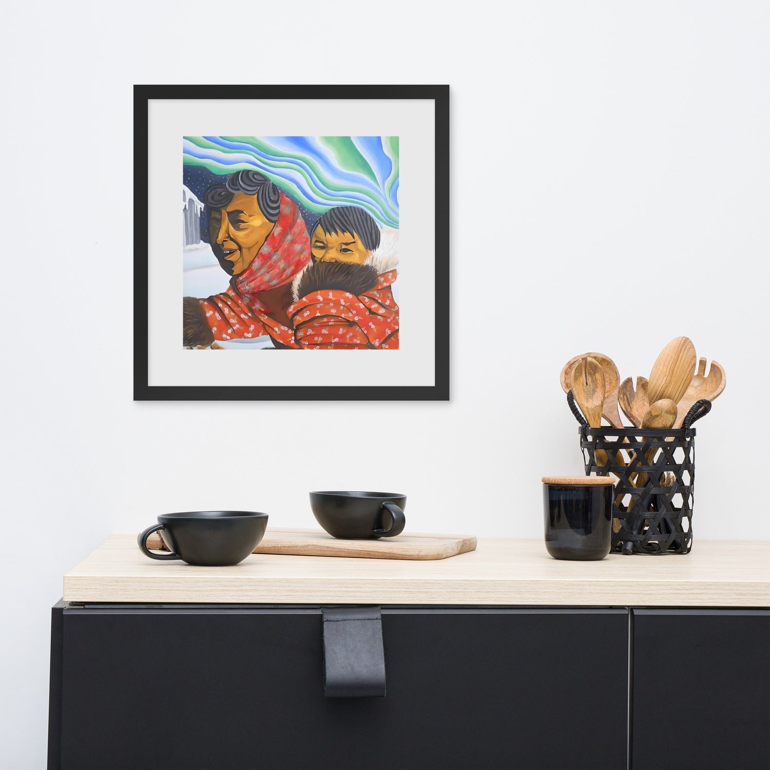 A kitchen counter with a wood top, black utensils and a picture of a native Alaskan with her son walking through the snow at night. The Northern Lights behind her in the sky.