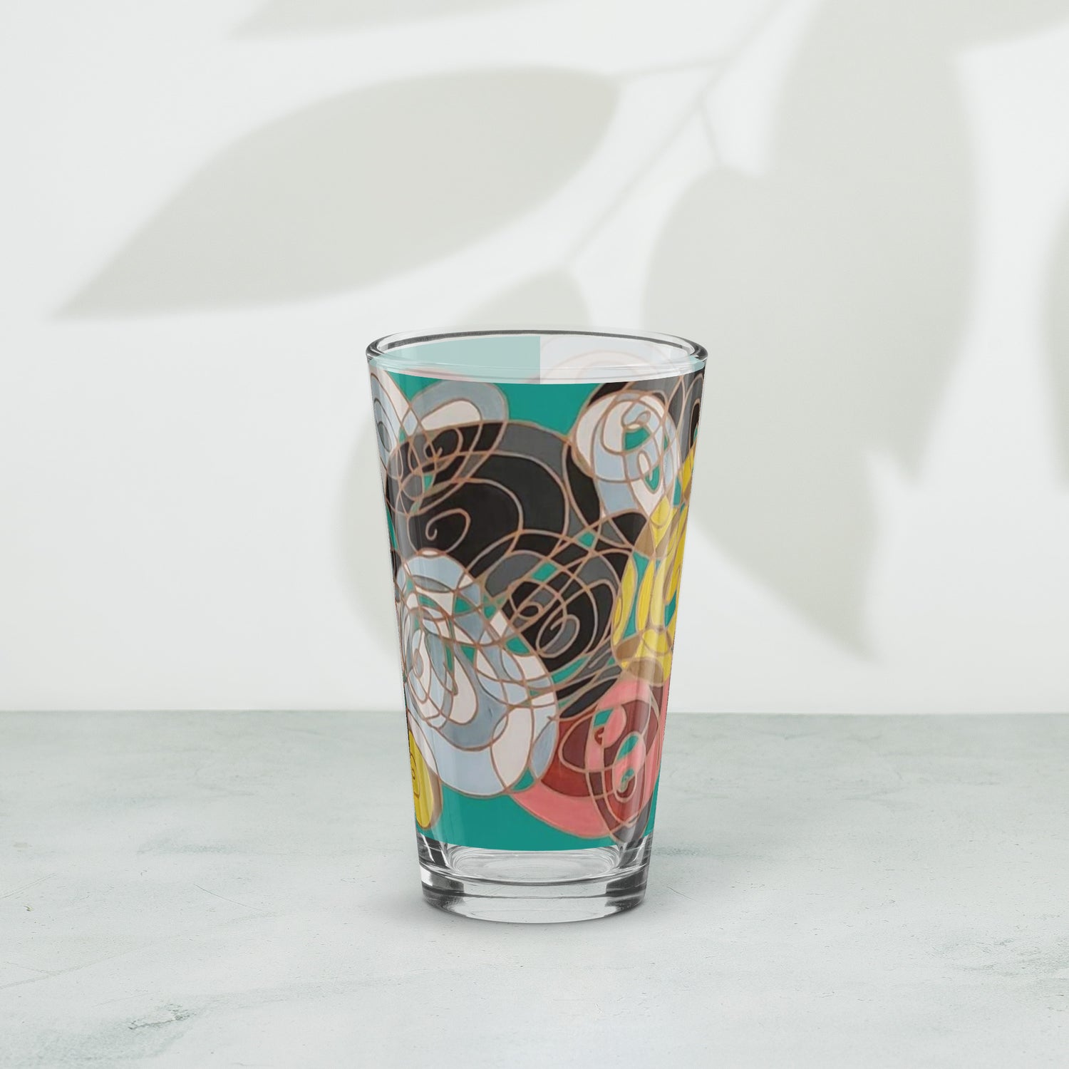 A drinking glass featuring abstract swirl art in red, yellow, black, white and teal.